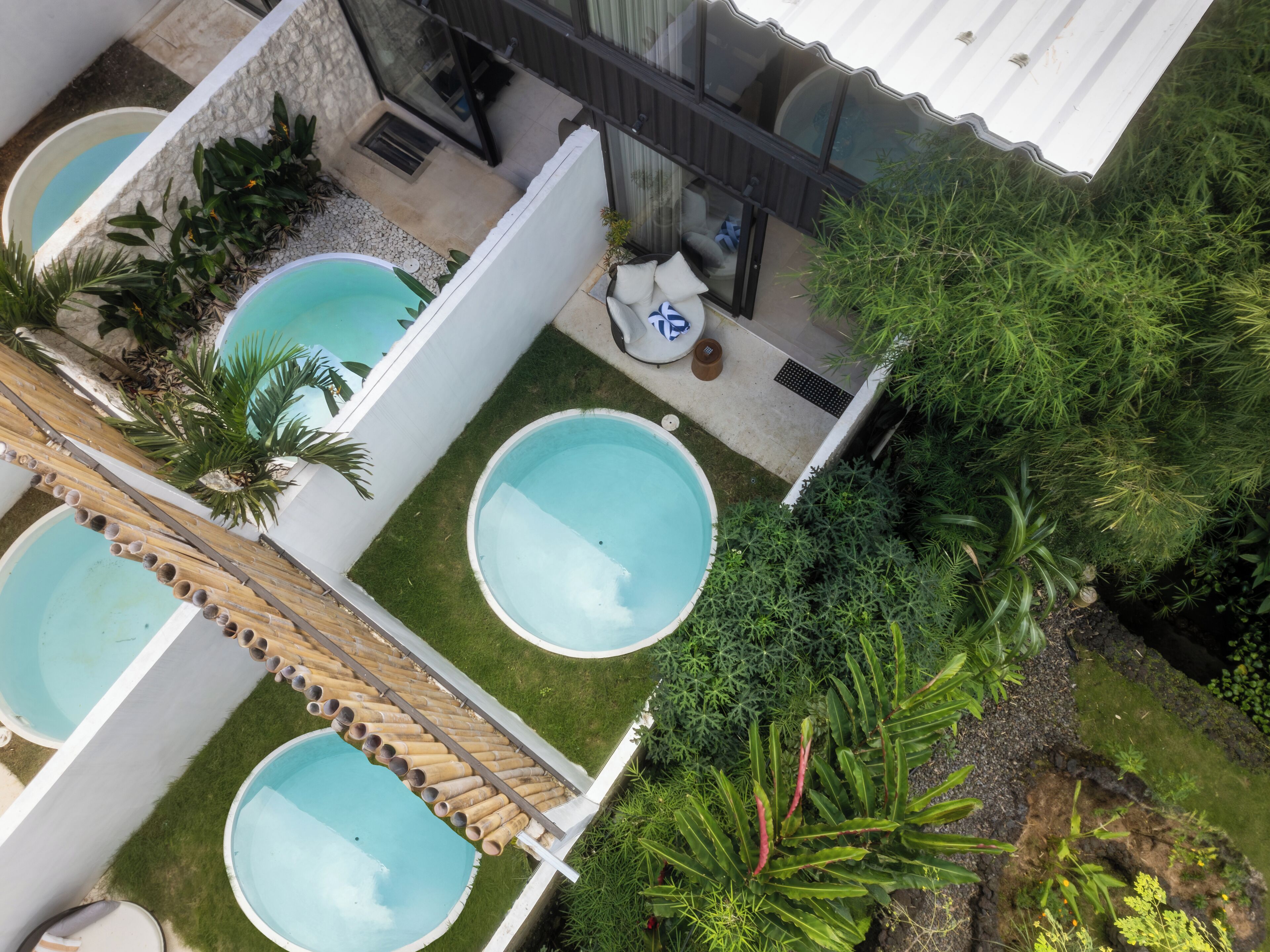Un espace piscine sur le toit, comprenant trois piscines, entouré d’une végétation luxuriante et agrémenté d’un petit coin salon.