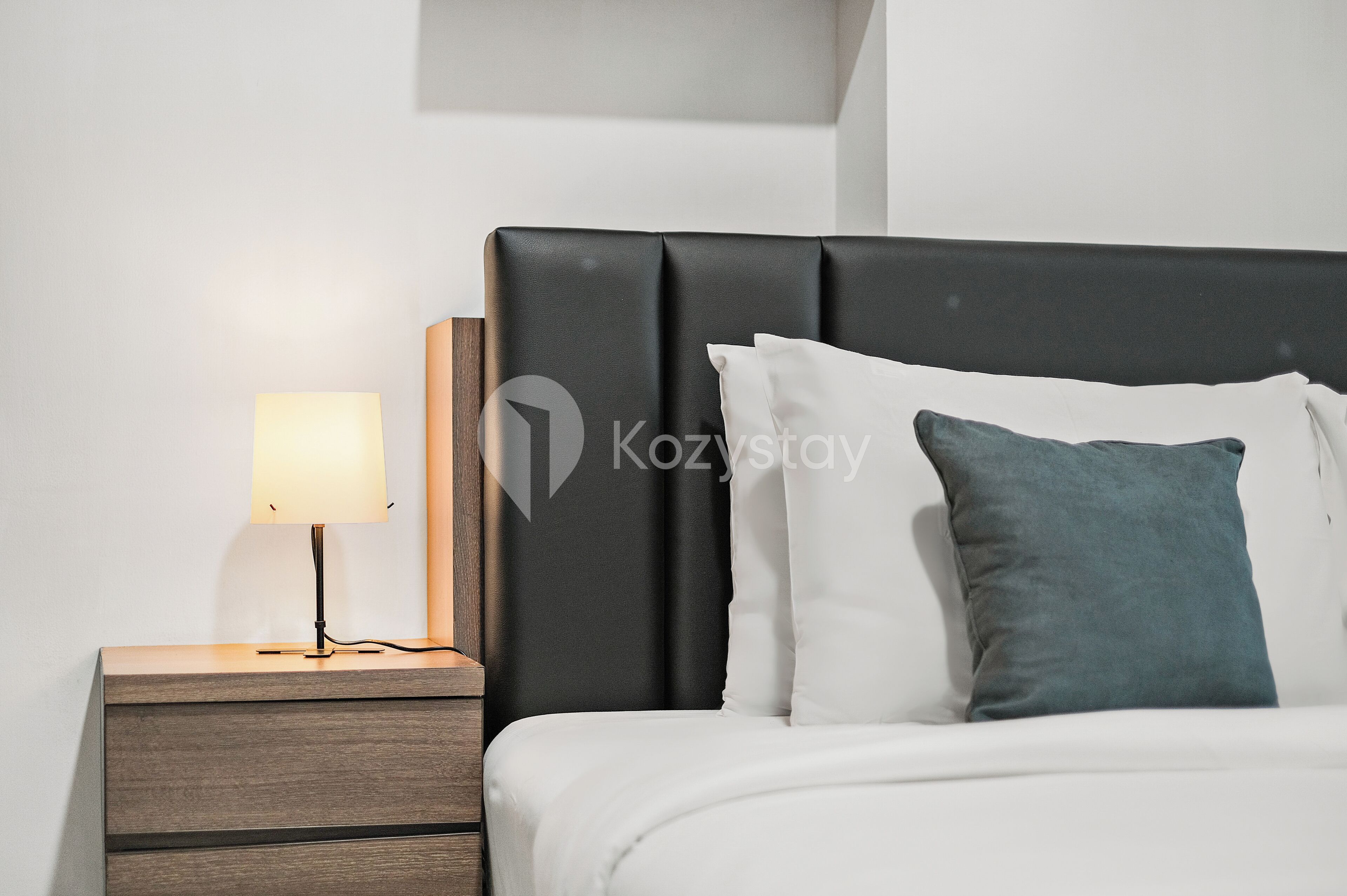 A modern hotel room with a bed, a nightstand, a lamp, and a wall-mounted artwork.