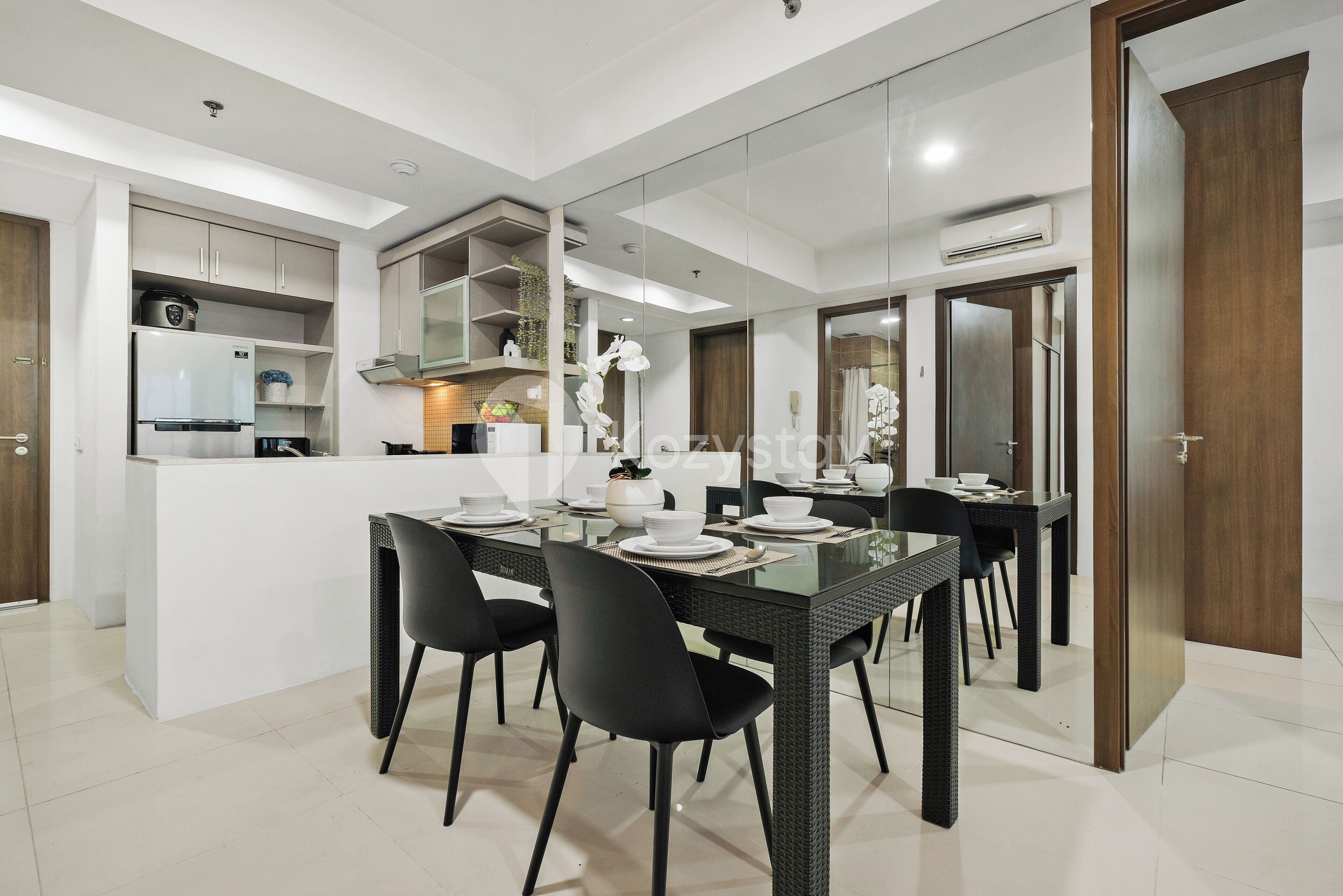 Une cuisine moderne avec des armoires blanches, un four encastré et un coin repas comprenant une table en verre et des chaises noires.