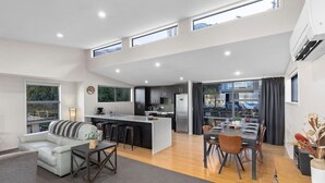 A modern open-plan living area with a kitchen, dining space, and a sofa. - Mountain Views on Sainsbury (Queenstown)