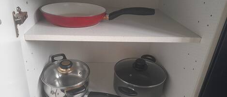 Una estantería de cocina con una sartén roja, una olla de acero inoxidable con tapa y otra olla con tapa.