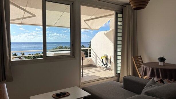 A balcony with a view of the ocean, a sofa, a table, and a hanging light fixture. - Charming 1-bedroom apartment in lovely Papeete entrance. (Unknown)