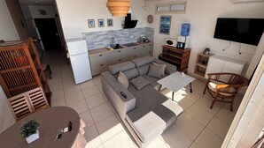 A compact living space with a kitchenette, grey sofa, dining table, and a TV mounted on the wall. - Charming 1-bedroom apartment in lovely Papeete entrance. (Unknown)