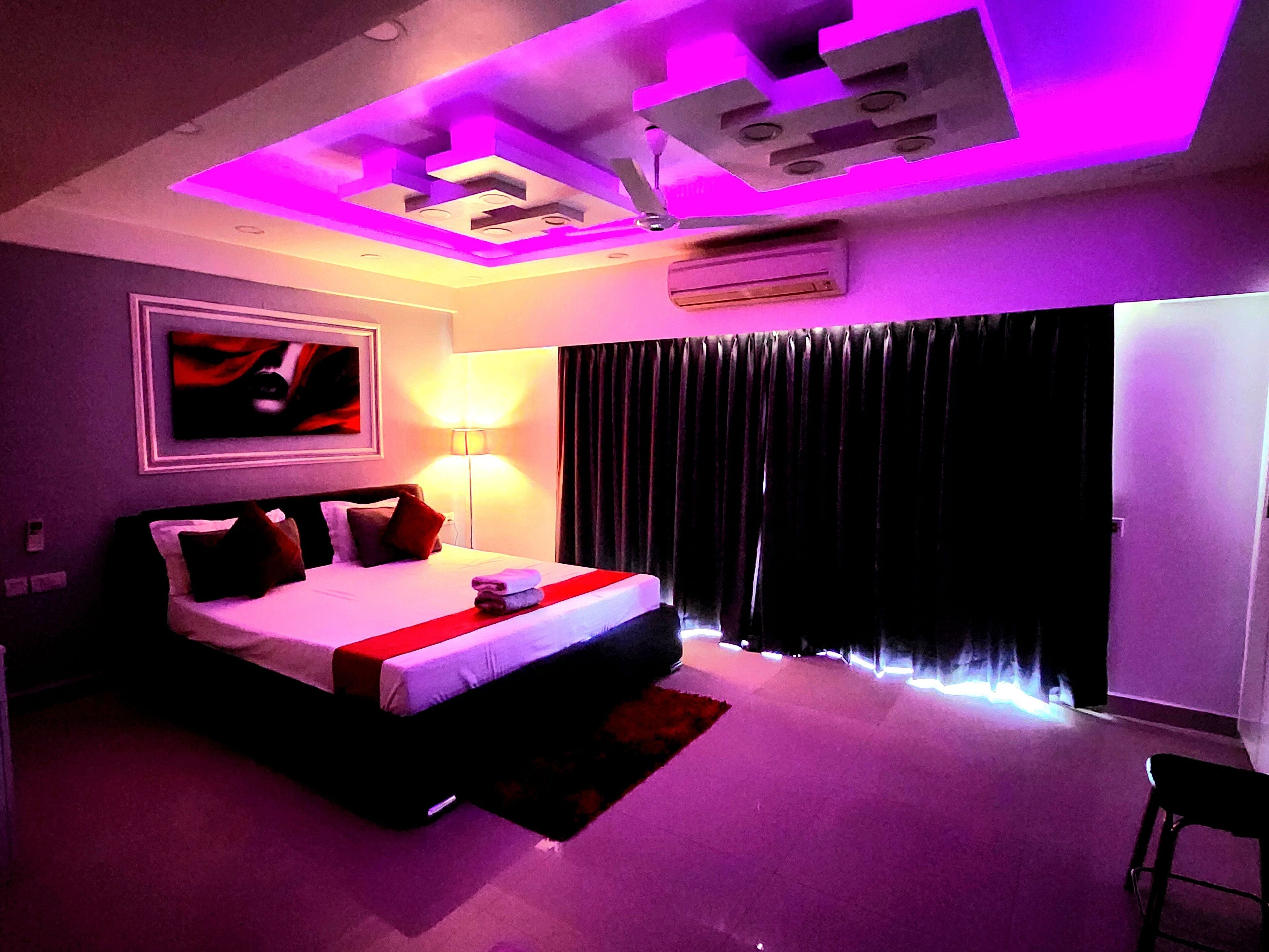 Een moderne hotelkamer met een groot bed, een flatscreen televisie, een luchtverkoeler in het plafond en een raam met donkere gordijnen.
