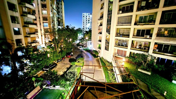 A nighttime view of a multi-story residential building with balconies, a central pathway, and surrounding greenery. - Xanadu Studio Apartment # 902 (Kolkata)