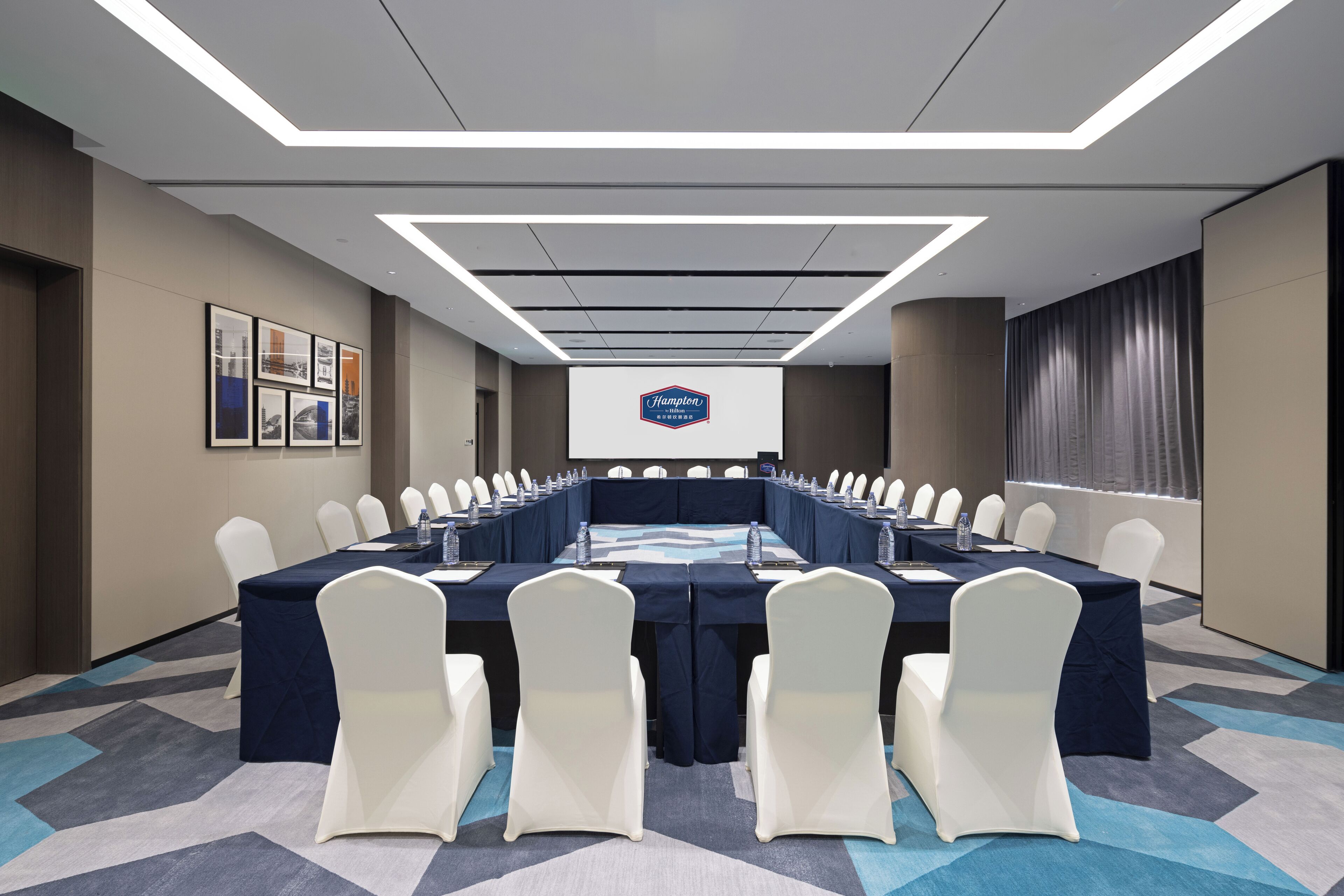 A conference room with a long table, white chairs, and a Hampton's logo on the wall.