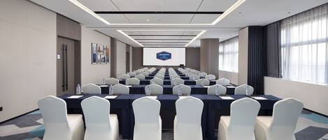 A conference room with a long table, white chairs, and a large screen displaying a logo.