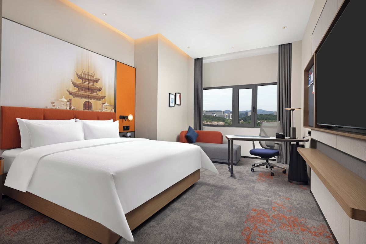 Une chambre d’hôtel moderne dotée d’un grand lit, d’un bureau et offrant une vue sur la ville grâce à de grandes fenêtres.