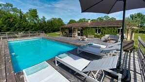A swimming pool with lounge chairs and an umbrella, surrounded by a wooden deck and a house with a tiled roof. - Maison les comtes - with swimming pool in Périgord (Sainte-Radegonde)
