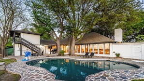 A swimming pool with stone tiles, a covered patio, and a staircase leading to a second level.