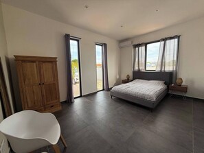 A bedroom with a bed, a wardrobe, a chair, and a balcony with curtains. - Villa Milamor Curacao - Harmonie, Grote Berg (Grote Berg)