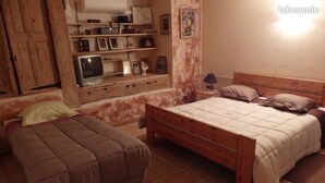 Un dormitorio con una cama de madera, una mesita de noche, un televisor y una estantería con objetos personales.