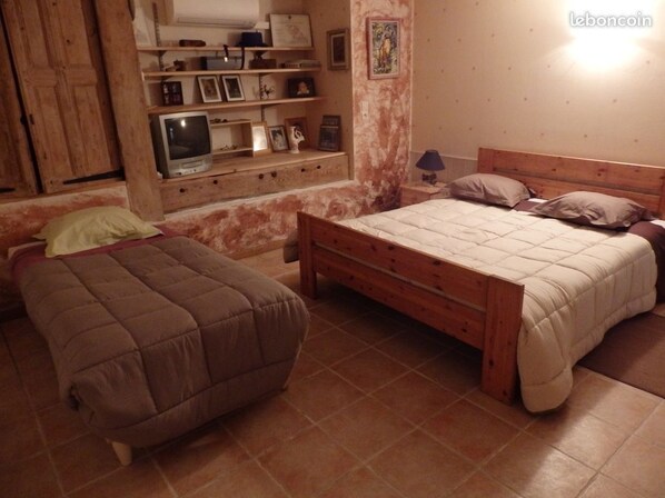 A bedroom with a wooden bed, a bedside table, a TV, and a shelf with personal items.
