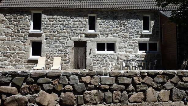 Una casa de piedra con techo de tejas, varias ventanas y un muro de piedra en primer plano.
