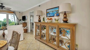 A living room with a wooden cabinet, white chairs, a dining table, and a ceiling fan. - Sail Inn SaintSimons-ground unit,beach access,pool (St. Simons Island)