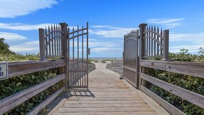 A wooden boardwalk leading to a gated entrance with a clear view of the beach and ocean in the distance. - Sail Inn SaintSimons-ground unit,beach access,pool (St. Simons Island)