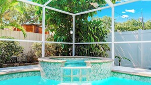 A swimming pool with a hot tub, surrounded by a white fence and lush greenery.