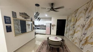 Un salon moderne avec un mur à motifs de marbre, un ventilateur de plafond, un coin repas avec une table et des chaises, et une cuisine en arrière-plan.