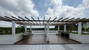 Un espace extérieur aménagé en patio, doté d’une pergola, d’un sol carrelé et de jardinières en béton.