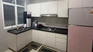 Une cuisine compacte avec des meubles blancs, une hotte de cuisinière en acier inoxydable, un évier et un réfrigérateur.