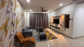 Un salon moderne avec un canapé, un pouf et un fauteuil à bascule. Un téléviseur à écran plat est fixé au mur, et il y a un ventilateur de plafond.