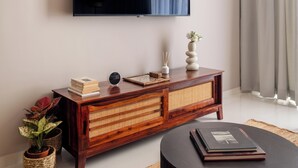 Una sala de estar moderna con un televisor de pantalla plana montado en la pared, una mesa consola de madera con libros y objetos decorativos, una mesa de centro redonda negra y una alfombra tejida en el suelo.