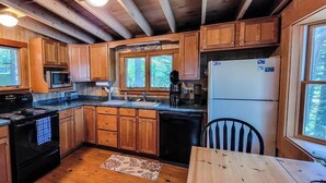 Cocina de cabaña de madera con estufa, microondas, lavamanos y refrigerador.