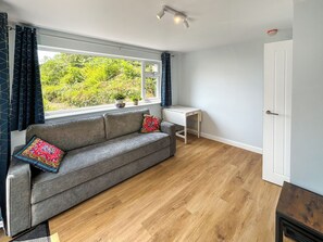 A room with a grey sofa, a small white desk, a window with curtains, and a door. - 2 bedroom accommodation in Boscombe, near Bournemouth (Boscombe, near Bournemouth)