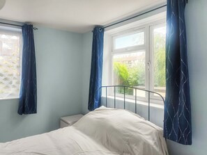 A bedroom with a bed, a nightstand, and a window with curtains.