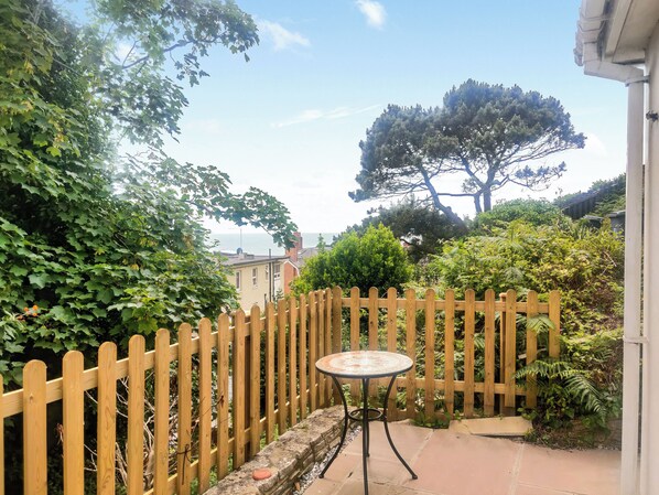 A wooden fence, a round table, and a view of a tree and buildings in the background.