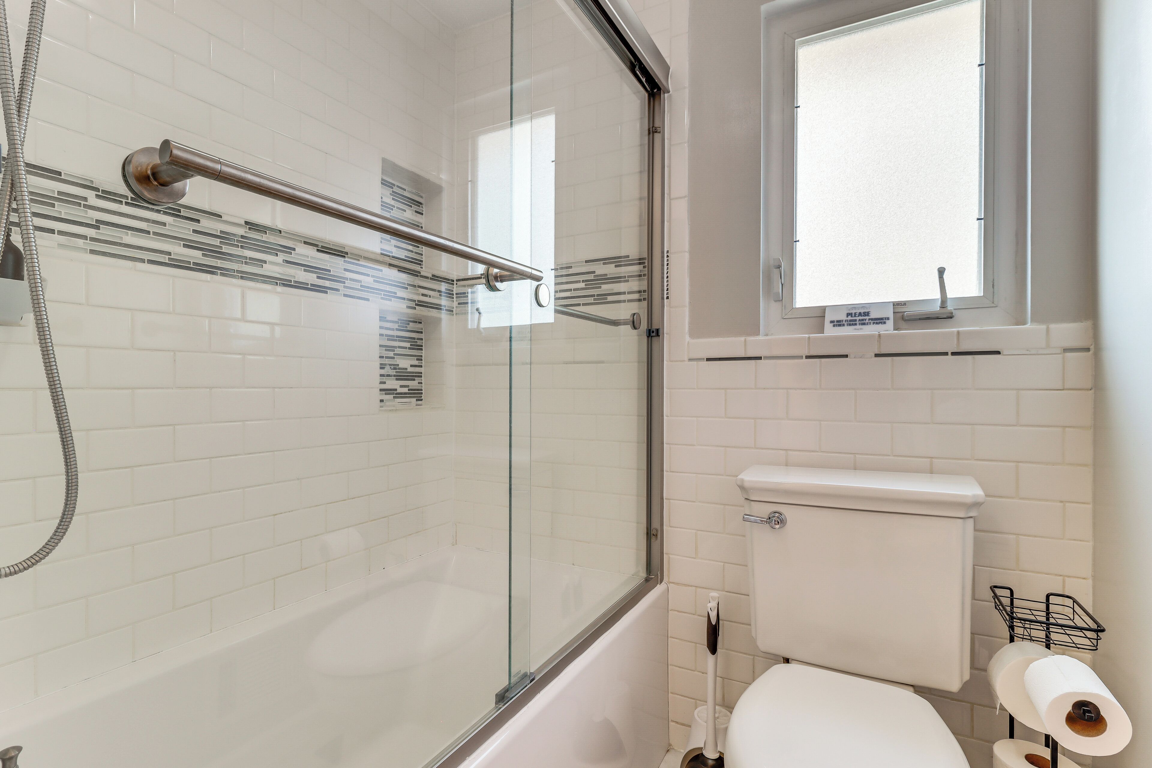 A modern bathroom with a glass-enclosed shower, a white toilet, and a window above the toilet.