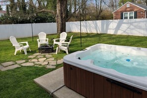 Un jardin avec un jacuzzi, un chemin de pierres et des chaises blanches.