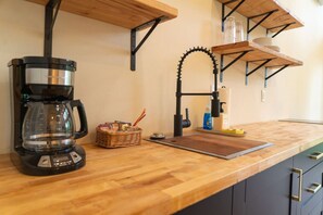 A kitchen with a coffee maker, a sink, and shelves with glass jars and plates.