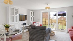 Una sala de estar moderna con un televisor de pantalla plana, muebles blancos y un ventanal corredizo que da a un jardín trasero.