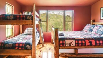 Una habitación con dos literas, suelo de madera y grandes ventanas que dan a árboles.