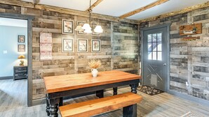 Ein rustikaler Essbereich mit Holztisch und Bank, gerahmten Postern an der Wand und einer Tür mit Fenster.