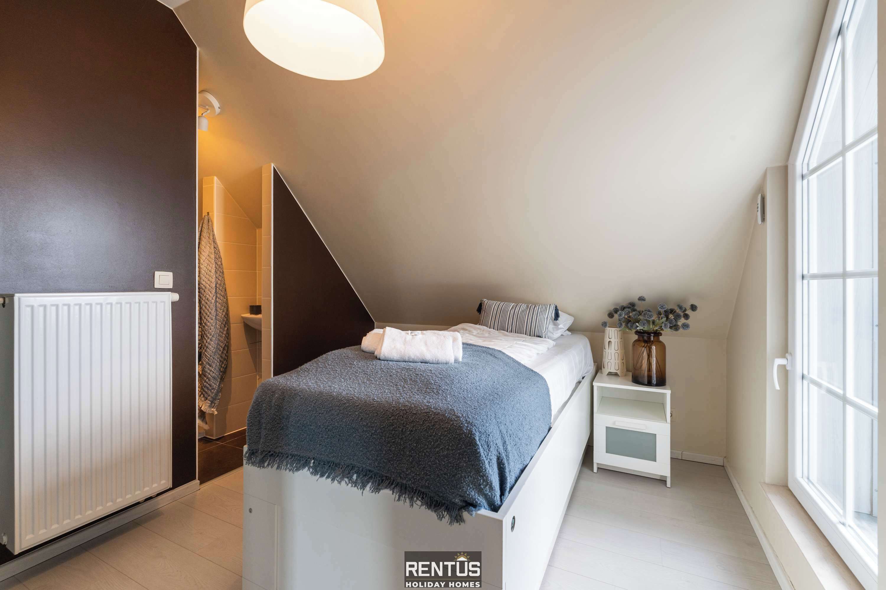 Een slaapkamer met een bed, nachtkastje, radiator, raam en deur.