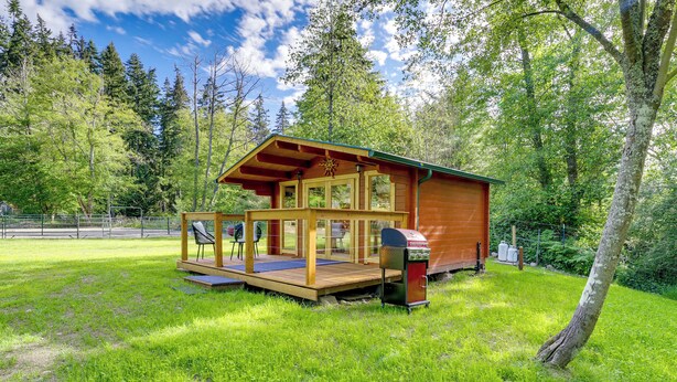 A wooden cabin with a deck, surrounded by lush greenery and trees. - On Hobby Farm: Whidbey Island Tiny Home (Clinton)