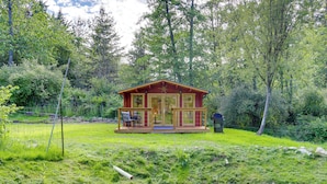 A cabin with a porch, a small deck, and a view of the surrounding forest. - On Hobby Farm: Whidbey Island Tiny Home (Clinton)