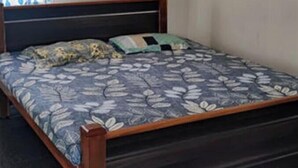 Un lit simple avec une couvre-lit à motifs floraux, une tête de lit en bois et une fenêtre ornée de rideaux bleus et blancs.