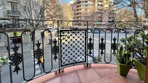 A balcony with a wrought iron railing, a potted plant, and a view of a street with buildings and trees. - Suite Miro Eixample Barcelona (Barcelona)