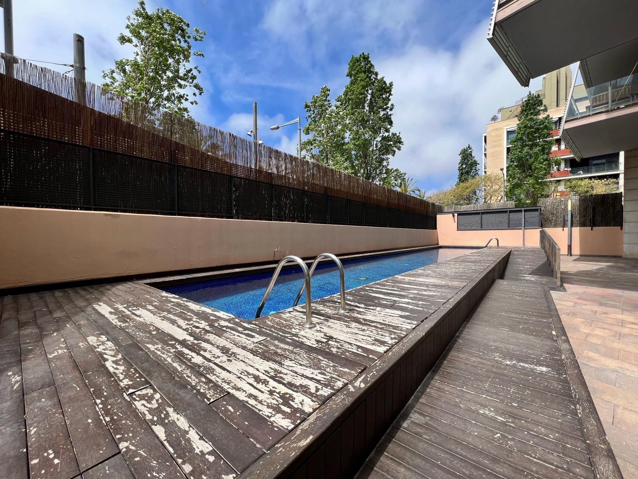 A swimming pool with a wooden deck, surrounded by a fence and trees.