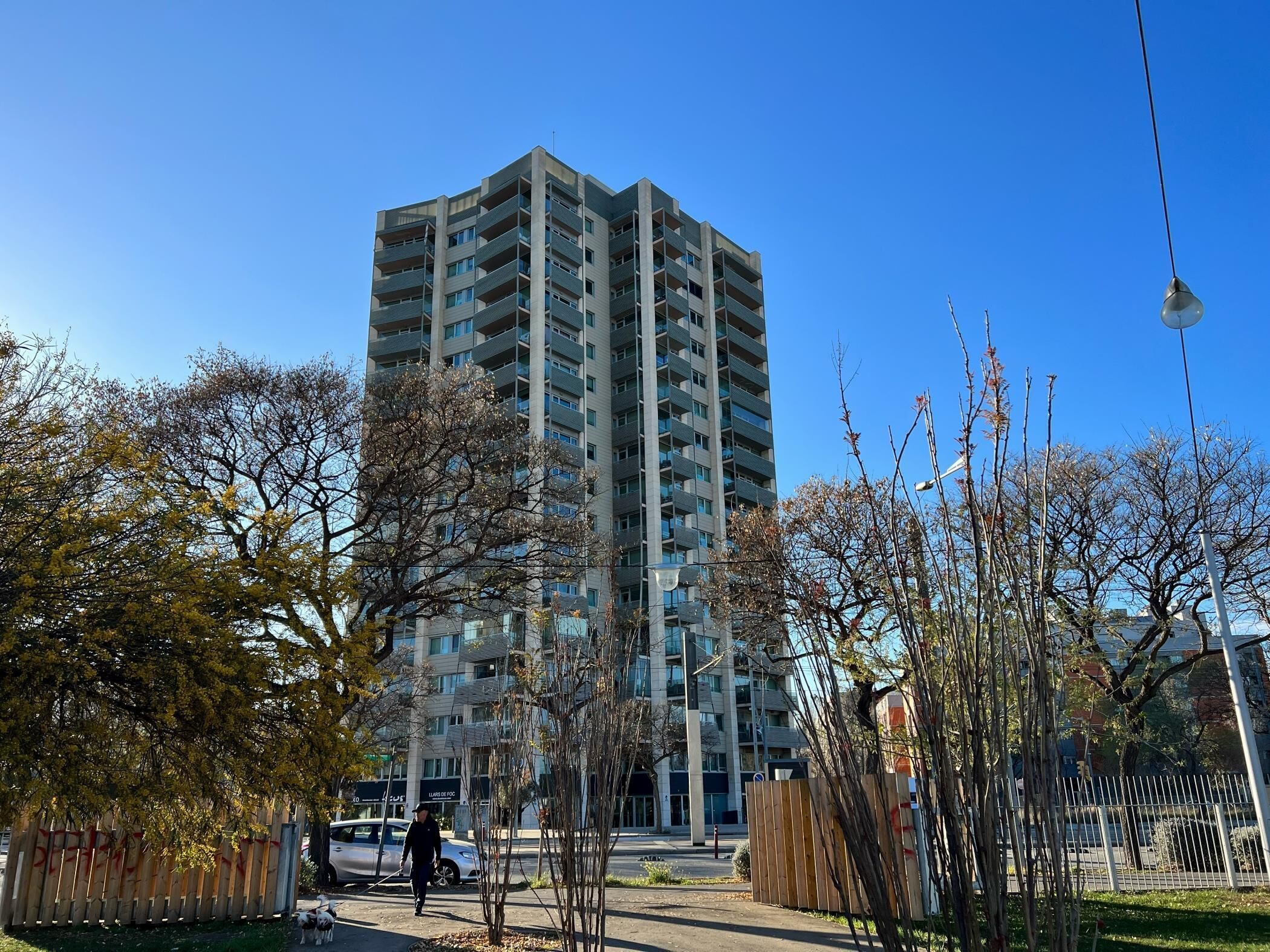 Un immeuble de grande hauteur doté de nombreux balcons, entouré d’arbres et d’une zone délimitée par une clôture.