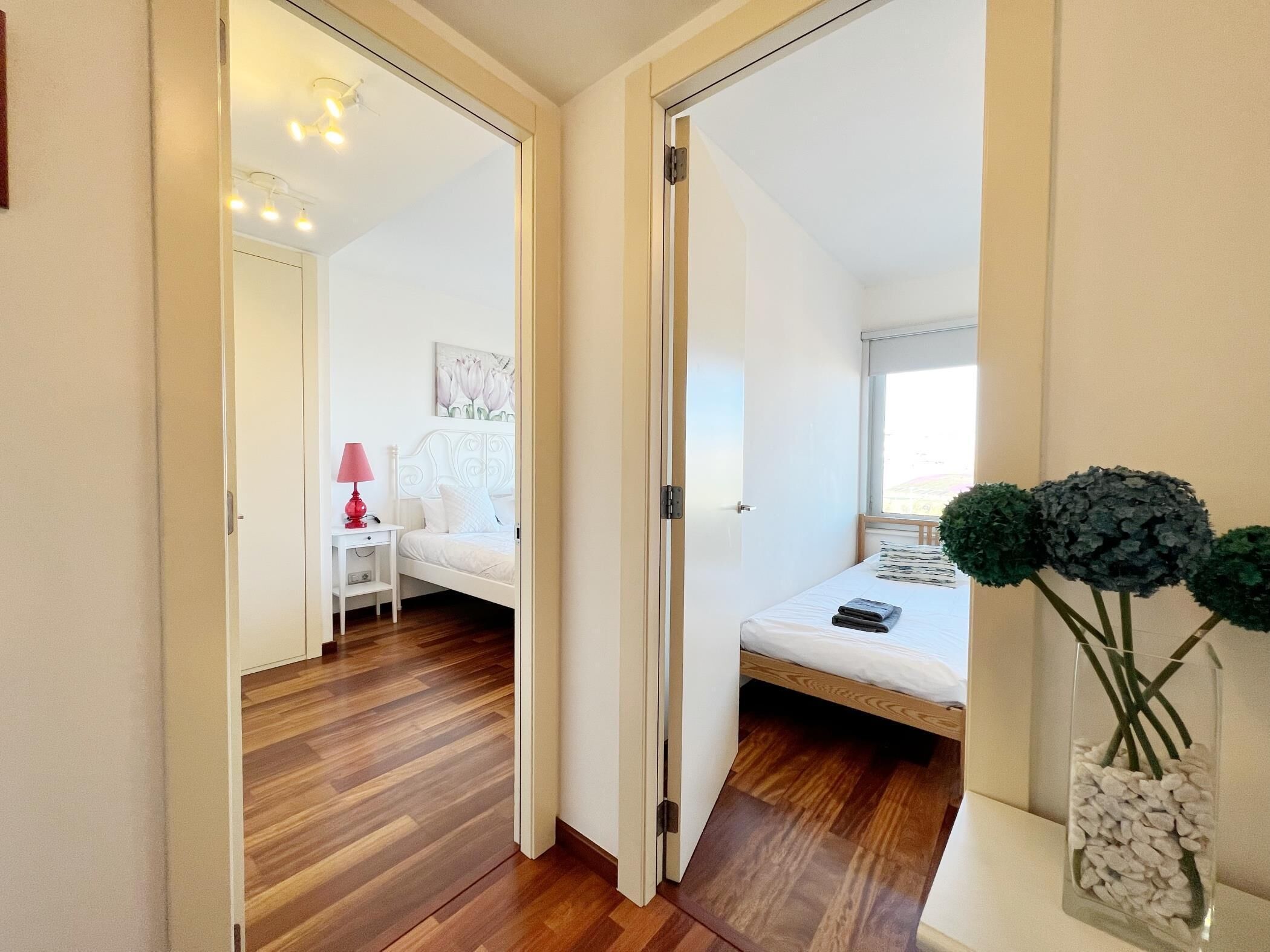 Une chambre avec un plancher en bois, un lit blanc, une table de chevet avec une lampe et une fenêtre donnant sur un beau paysage.