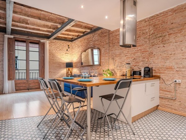A kitchen with a brick wall, wooden ceiling beams, and a central island with bar stools.