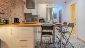 Una cocina moderna con pared de ladrillo, electrodomésticos de acero inoxidable y un comedor con mesa y sillas.