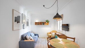 A modern living room with a sofa, a dining table with chairs, a TV, and a hanging light fixture.