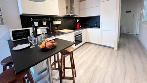 A modern kitchen with white cabinets, a black countertop, and a wooden dining table with stools.