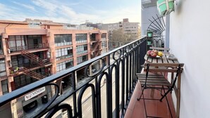 A balcony with a view of adjacent buildings, a small table with fruits, and a green bucket.