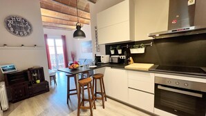 A modern kitchen with a central island, wooden stools, a built-in oven, and a hanging plant.